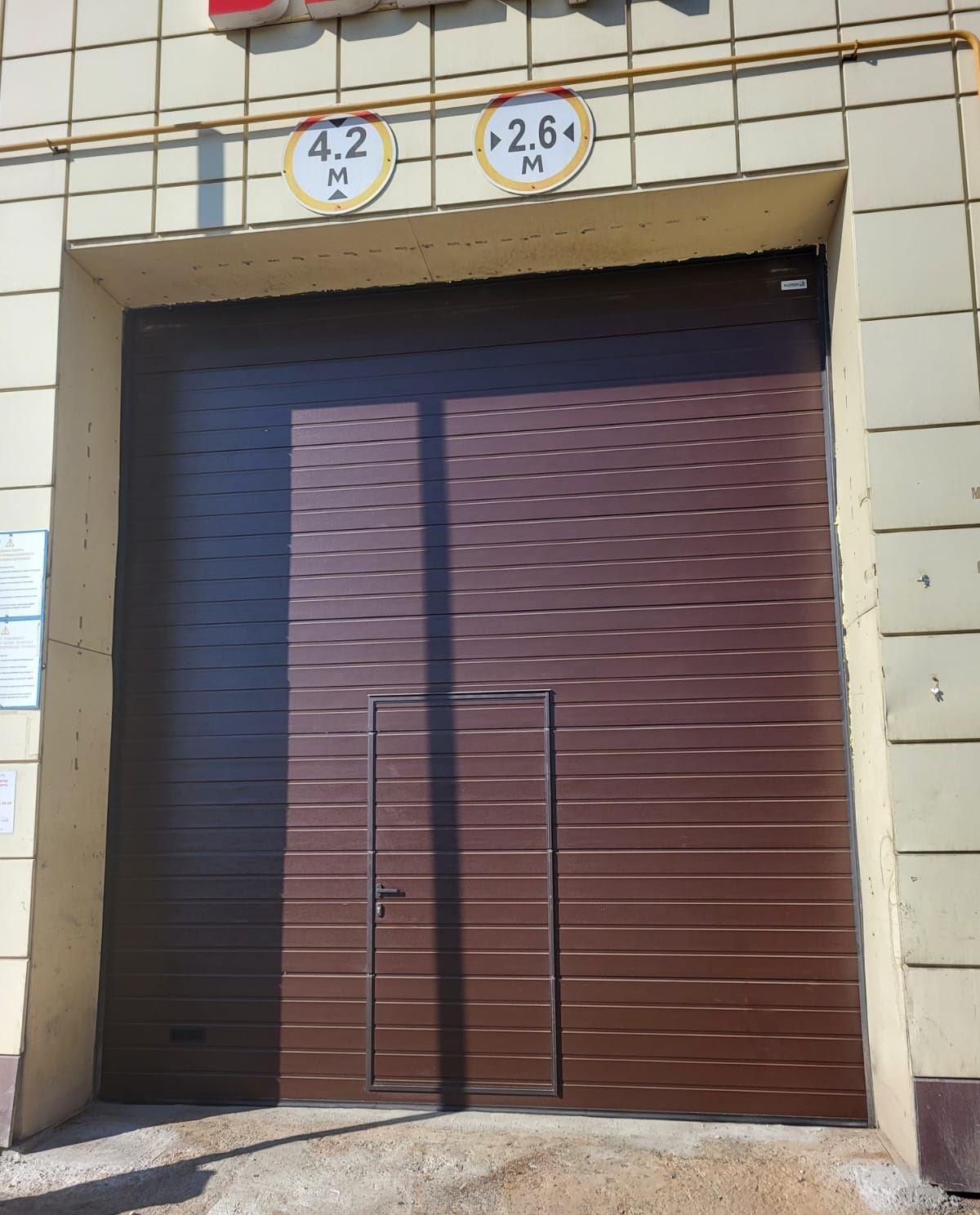Ғимарат қасбетіндегі кіші есігі бар қоңыр өнеркәсіптік секциялық қақпа